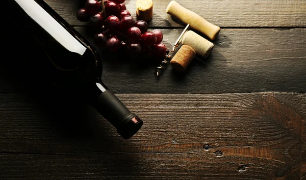 Botella de vino con tapones y uvas sobre fondo de mesa de madera — Foto de Stock