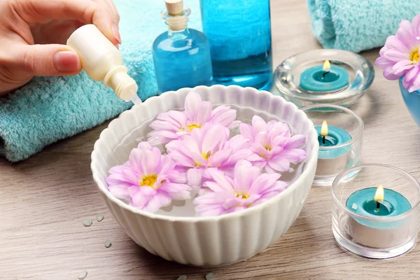 Female hand with bottle of essence and bowl of aroma spa water on wooden table, closeup — Stock Photo, Image