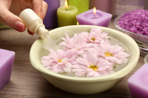 Mano femenina con botella de esencia y tazón de agua de spa aroma en mesa de madera, primer plano — Foto de Stock