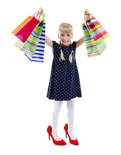 Belle petite fille dans les chaussures de maman avec des sacs à provisions isolés sur blanc — Photo