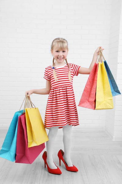 Hermosa niña en los zapatos de mamá con bolsas de compras en la habitación — Foto de Stock