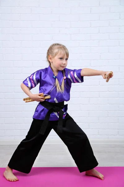 Menina em quimono fazendo exercícios com nunchaku no fundo da parede — Fotografia de Stock