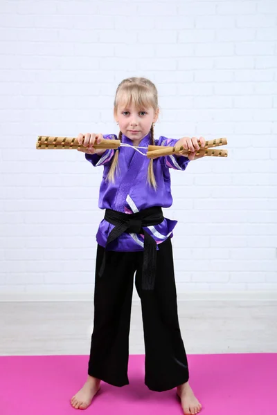 Menina em quimono fazendo exercícios com nunchaku no fundo da parede — Fotografia de Stock