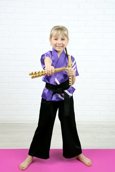 Kimono ile nunchaku duvar arka plan üzerinde yapıyor, küçük kız — Stok fotoğraf