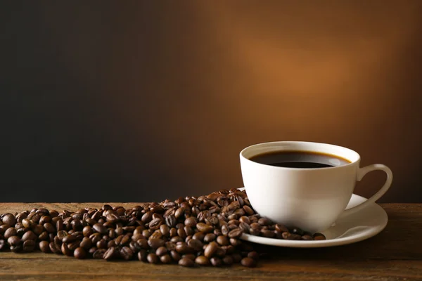 Taza de café con granos sobre mesa de madera sobre fondo oscuro — Foto de Stock