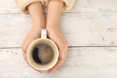 Kadın elleri bir fincan kahve tutuyor.