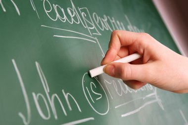 Teacher hand writing grammar sentences on blackboard background clipart