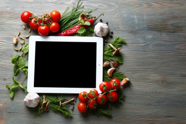 Taze otlar, domates ve baharat ahşap arka plan üzerinde dijital tablet