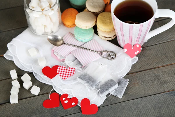 Herzförmige Teebeutelanhänger, Makronen und Tasse Tee auf Holzgrund — Stockfoto