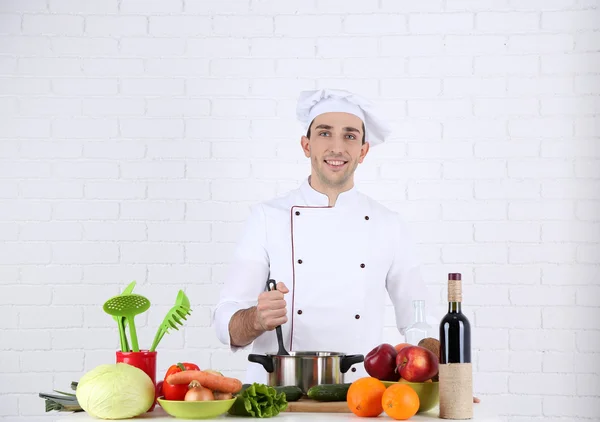 Chef at table with different products and utensil in kitchen on white wall background — Stock Photo, Image