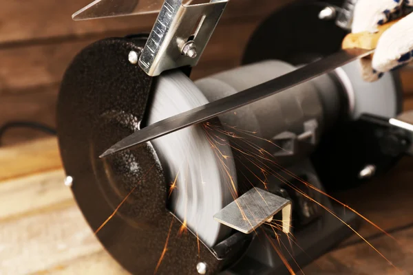 Knife sharpener and hand with blade on wooden table, closeup — Stock Photo, Image