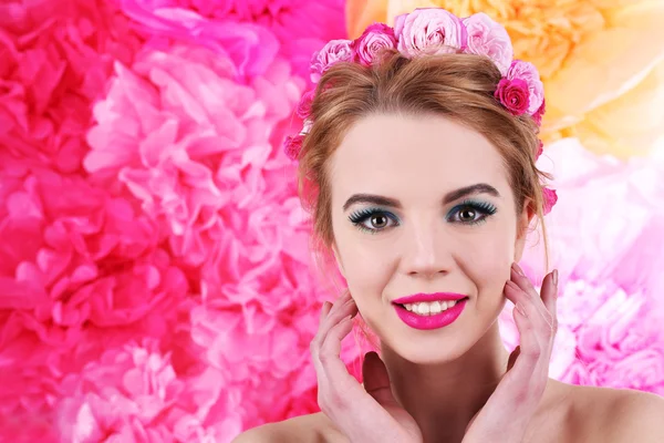 Portret młodej kobiety z kwiatami we włosach na jasnym tle różowy — Zdjęcie stockowe