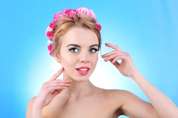 Portrait of young woman with flowers in hair on blue background — Stock Photo, Image