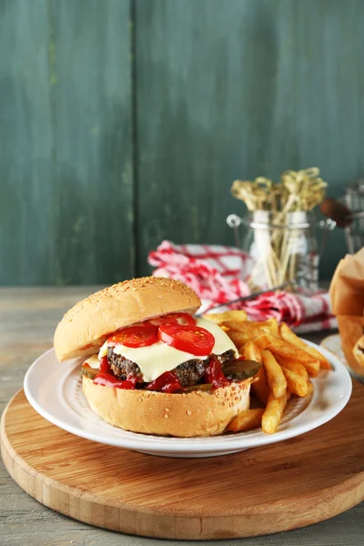 Hamburger savoureux et frites sur assiette, sur fond de bois. Concept d'aliments malsains — Photo