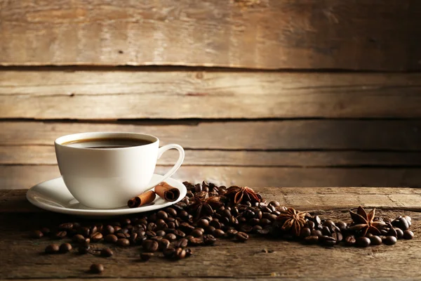Xícara de café com grãos e especiarias em fundo de madeira — Fotografia de Stock