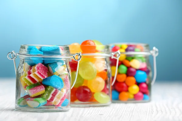 Coloridos caramelos en frascos sobre la mesa sobre fondo azul —  Fotos de Stock