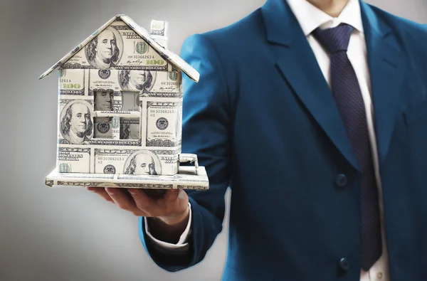 Model of house made of money in male hands on gray background — Stock Photo, Image