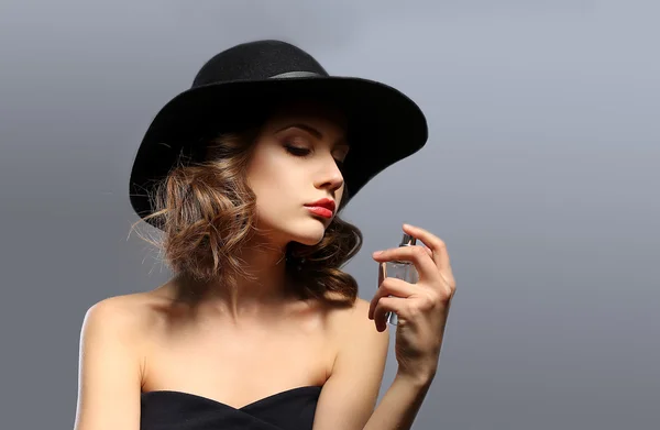Vacker kvinna med parfymflaska på grå bakgrund — Stockfoto