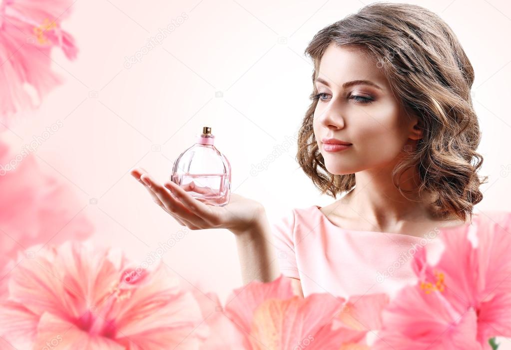 Beautiful woman with perfume bottle in flowers on pink background
