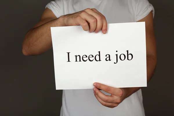 Blad papier met inscriptie ibehoefte een baan in mannelijke handen op donkere achtergrond — Stockfoto