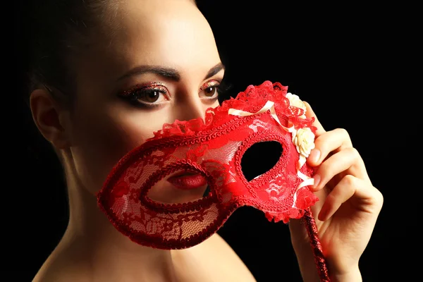 Portrait of beautiful woman with fancy glitter makeup and masquerade mask on dark background