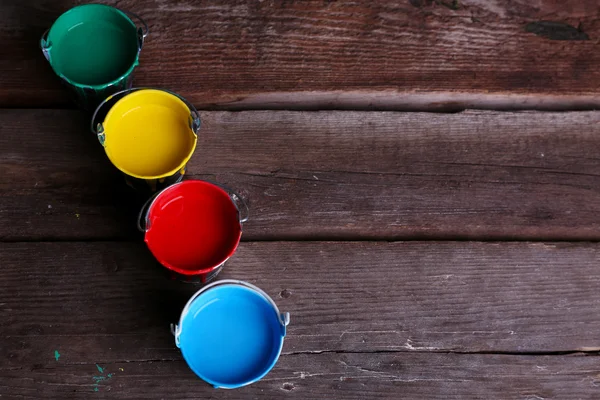 Metal buckets with colorful paint on wooden background — Stock Photo, Image