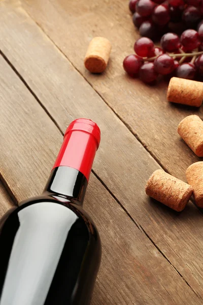 Botella de vino con tapones y uvas sobre fondo de mesa de madera — Foto de Stock