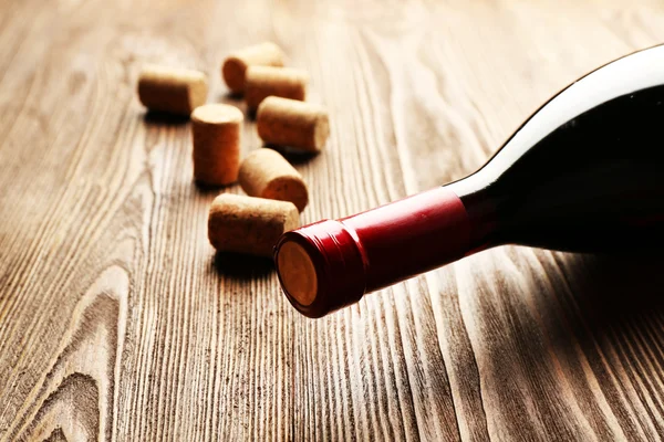 Glass bottle of wine with corks on wooden table background — Stock Photo, Image