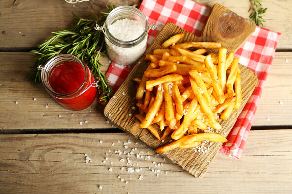 Tasty french fries on cutting board, on wooden table background
