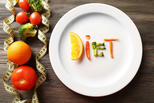 Word DIET made of sliced vegetables in plate with measuring tape on wooden table, top view — Stock Photo, Image