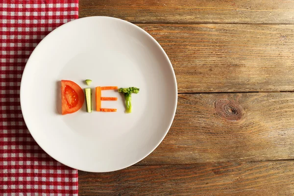 Word DIET made of sliced vegetables in white plate with napkin on wooden background — Stock Photo, Image