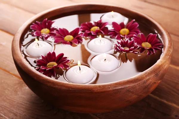 Bowl of spa water with flowers and candles on wooden table, closeup — Stock Photo, Image