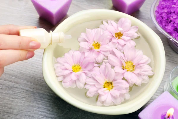 Mano femenina con botella de esencia y tazón de agua de spa aroma en mesa de madera, primer plano — Foto de Stock