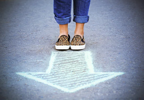 Женские ноги и рисунок стрелки на фоне тротуара — стоковое фото