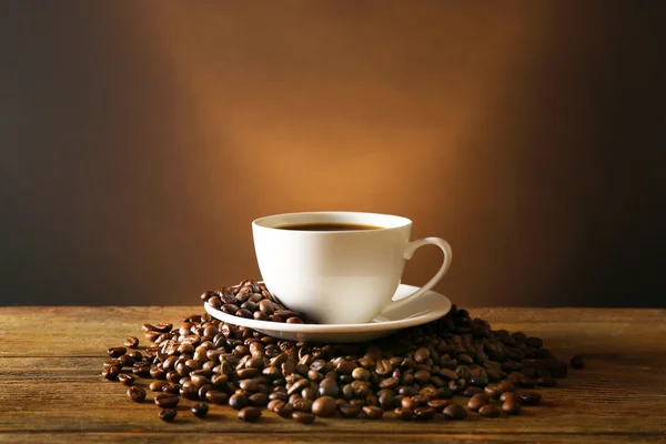 Kopje koffie met korrels op houten tafel op donkere achtergrond — Stockfoto