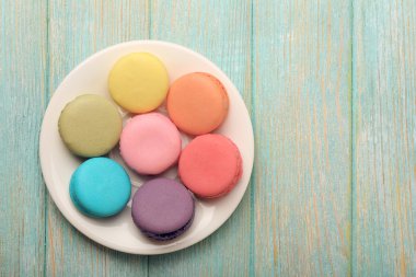 Renk ahşap arka plan üzerinde küçük tabak lezzetli renkli macaroons