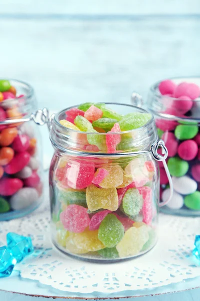 Mehrfarbige Bonbons in Glasgefäßen auf farbigem Holzhintergrund — Stockfoto