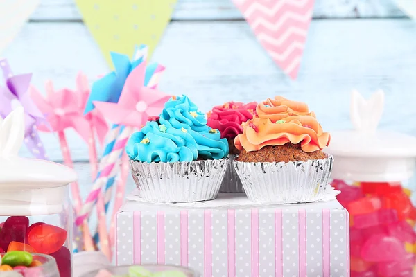 Caramelos multicolores en frascos de vidrio y cupcakes sobre fondo de madera de color — Foto de Stock