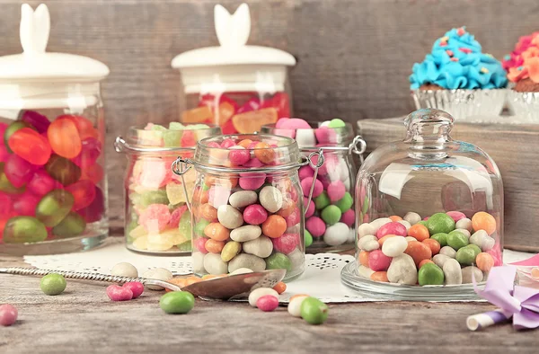 Multicolor snoepjes in glazen potten en cakejes op houten achtergrond — Stockfoto
