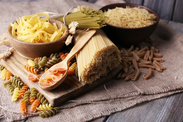 Different types of pasta on sackcloth on wooden background — Stock Photo, Image