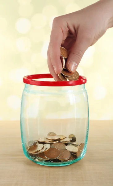 Female hand putting coins in glass bottle on bright background — Stock Photo, Image