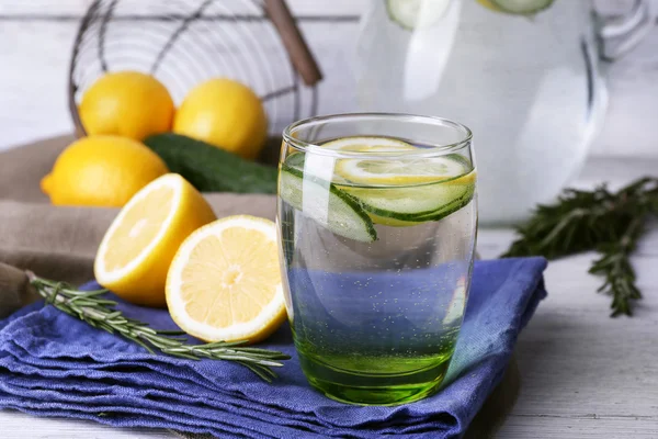 Fresh water with lemon and cucumber in glassware on napkin on wooden table, closeup — Stock Photo, Image