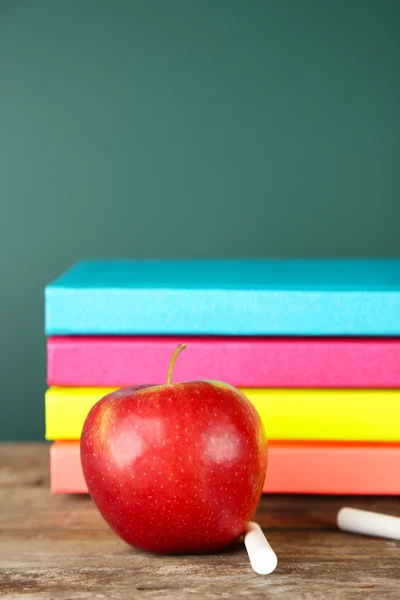Books, apple and chalk on blackboard background — Stock Photo, Image