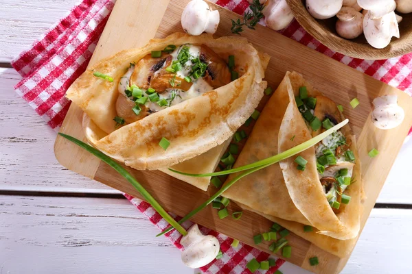 Pancakes with creamy mushrooms on cutting board on wooden table, top view — Stock Photo, Image