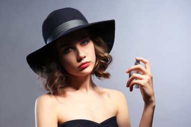 Gri arka planda parfüm şişesi olan güzel bir kadın.