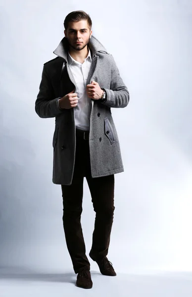 Молодой человек в пальто на сером фоне — стоковое фото