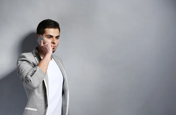 Young man with mobile phone on gray background — Stock Photo, Image
