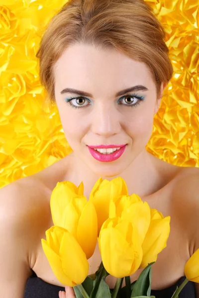 Portrait of young woman with tulips on yellow background — Stock Photo, Image