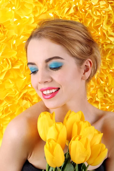 Portrait of young woman with tulips on yellow background — Stock Photo, Image