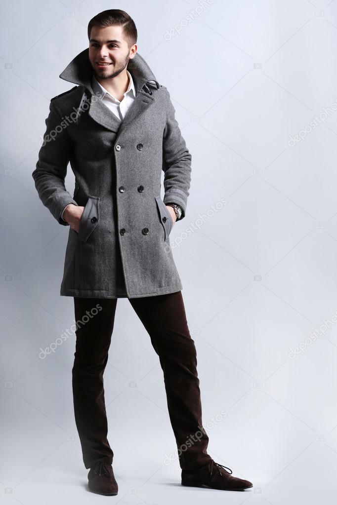 Young man in coat on gray background